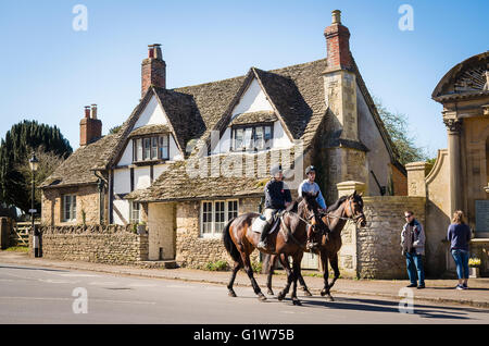 Deux horsefiders équitation à travers le village de Lacock Banque D'Images