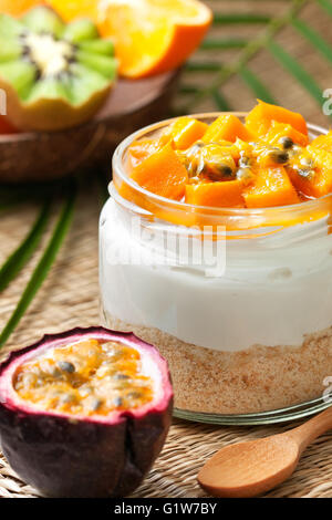 Cheesecake dans un pot avec des fruits tropicaux : mangue, fruit de la passion. Tranches de kiwi, orange et fruit de la passion sur fond de paille Banque D'Images