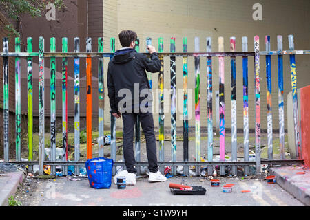 Man painting graffiti sur les poteaux de clôture par le tunnel à Leake Street, Waterloo, Londres en avril Banque D'Images