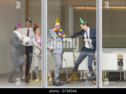 Les gens d'affaires de ludique party hats dancing fenêtre salle de conférence Banque D'Images