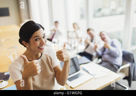 Portrait confident businesswoman et collègues gesturing thumbs-up dans la salle de conférence Banque D'Images