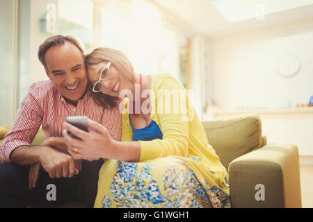 Smiling mature woman texting with cell phone in living room Banque D'Images
