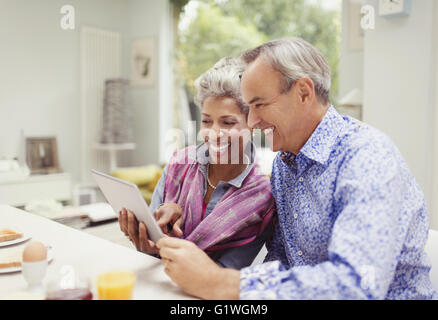 Smiling mature couple sharing digital tablet at breakfast table Banque D'Images