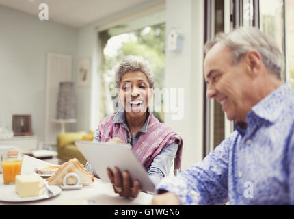 Mature couple laughing and using digital tablet at breakfast table Banque D'Images