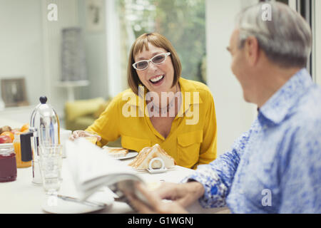 Smiling mature couple reading newspaper at breakfast table Banque D'Images
