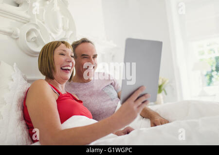 Laughing woman using digital tablet in bed Banque D'Images
