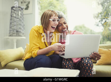 Rire femmes matures partageant un ordinateur portable sur salon canapé Banque D'Images