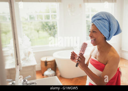 Maturité ludique woman singing into hairbrush dans salle de bains Banque D'Images