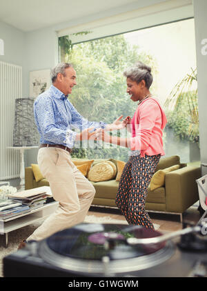 Playful young couple dancing derrière record player in living room Banque D'Images