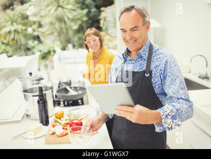 Young couple with digital tablet cooking in kitchen Banque D'Images