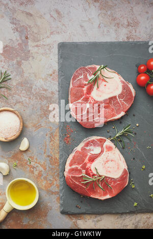 Jarret de veau de matières premières. Jarret de veau coupe brute sur ardoise en pierre avec le romarin et les ingrédients pour faire Osso Buco. Banque D'Images