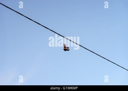 Vieille paire de chaussures accroché sur le fil téléphonique contre le ciel bleu, concept de changement de vie Banque D'Images