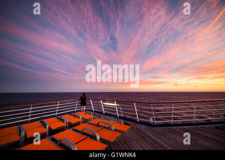 Chaises longues orange sur un vase navire contre un coucher de soleil de couleur orange. Banque D'Images