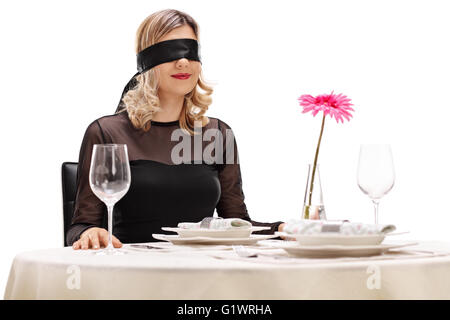 Jeune femme avec bandeau sur les yeux assis à une table de dîner romantique isolé sur fond blanc Banque D'Images