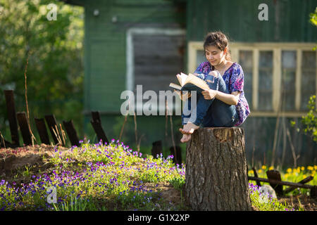 Teen girl lit livre assis sur une souche dans la cour d'une maison de campagne. Banque D'Images