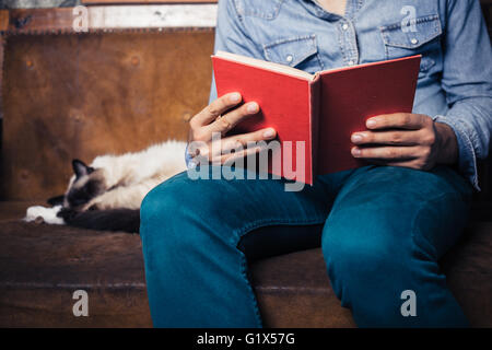 Un jeune homme est assis sur un canapé avec un chat et est en train de lire Banque D'Images