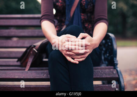 Une jeune femme est assise sur un banc de parc en automne Banque D'Images