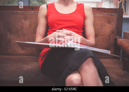 Une jeune femme est assise sur un canapé avec un classeur rempli de documents Banque D'Images