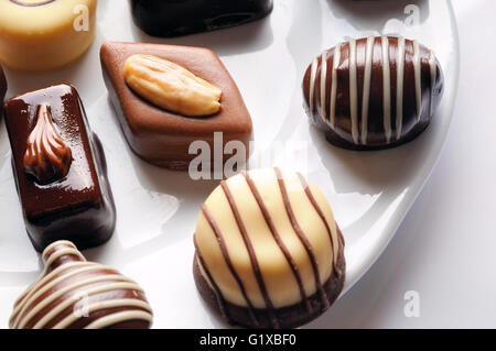 Assortiment de bonbons de chocolat noir et blanc avec les noix sur une plaque blanche sur un tableau blanc avec des morceaux de chocolat. Vue d'en haut. Fermer Banque D'Images