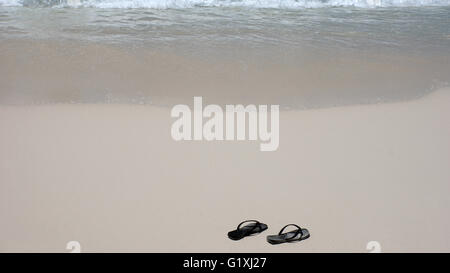 Chaussons noir sur une plage de sable blanc tropicales Banque D'Images