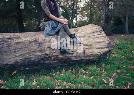 Une jeune femme est assise sur un grand arbre tombé dans le parc dans le cadre d'une journée ensoleillée d'automne Banque D'Images