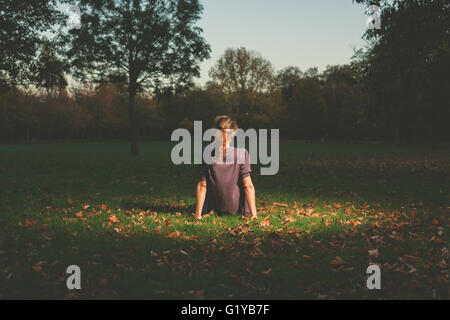 Une jeune femme est de l'emplacement sur l'herbe dans le parc le soir