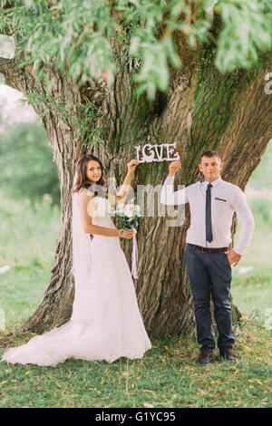 Happy married couple holding et fixation sur l'arbre des lettres mot amour standing in park Banque D'Images