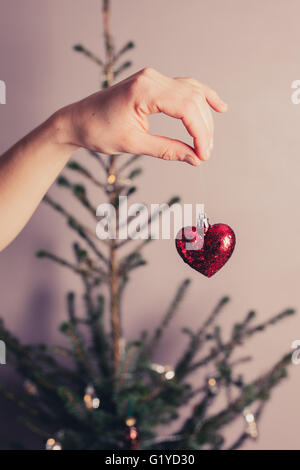 Une main tient un cœur décoratif par un arbre de Noël Banque D'Images