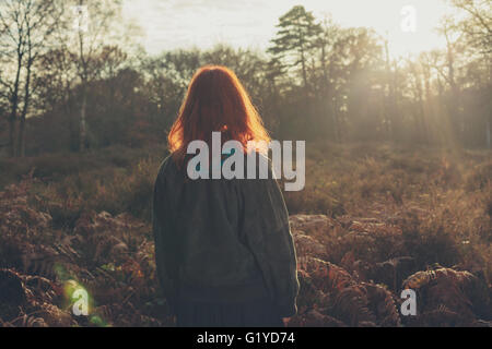 Une jeune femme se tient debout dans une forêt au coucher du soleil Banque D'Images