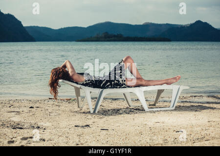 Une jeune femme est de vous détendre sur une chaise longue sur une plage tropicale Banque D'Images