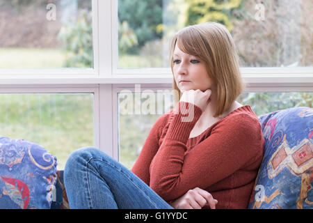 Jeune femme rousse solitaire est assis sur le canapé dans la véranda et elle est à l'avant. Banque D'Images