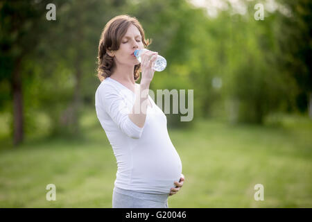 Portrait de jeunes femmes enceintes l'eau douce potable modèle aux yeux clos dans parc. Futur maman attend bébé holding bottle outdoor Banque D'Images