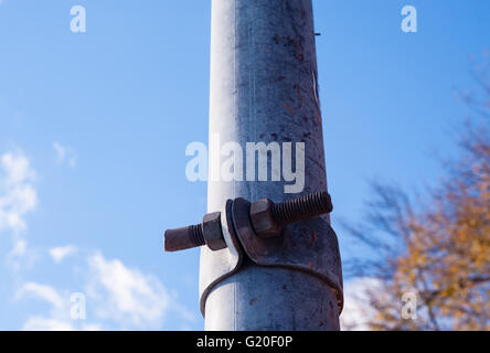 Dirty poteau de métal avec support fixé avec des vis rouillées, contre les troubles de ciel bleu et branches. Banque D'Images