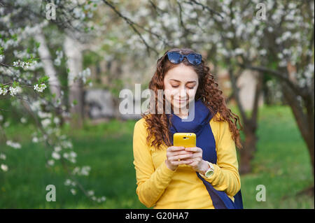 Jeune femme dans l'épanouissement Spring garden with smartphone Banque D'Images