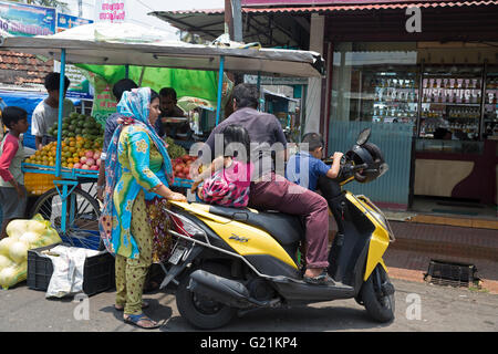 Une famille de quatre personnes s'asseoir sur un scooter à côté d'un étal de fruits à Cochin Inde Banque D'Images