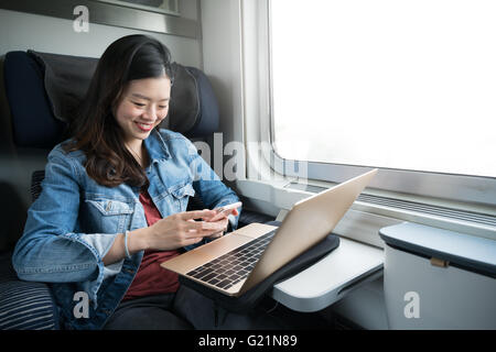 Asian woman smiling at smartphone avec un ordinateur portable sur le train, l'espace de copie sur la fenêtre Banque D'Images