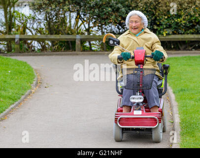 Heureux dame âgée équitation un scooter de mobilité dans un parc. Banque D'Images