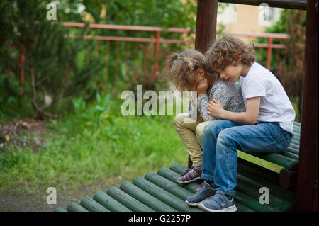 Deux enfants triste assis sur un banc dans la cour Banque D'Images