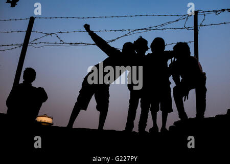 Silhouettes de garçons jouant sur un mur près de barbelés, Delhi, Inde Banque D'Images