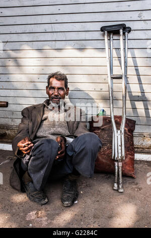 Homme assis sur la chaussée dans la vieille ville de Delhi, Inde avec des béquilles. Banque D'Images