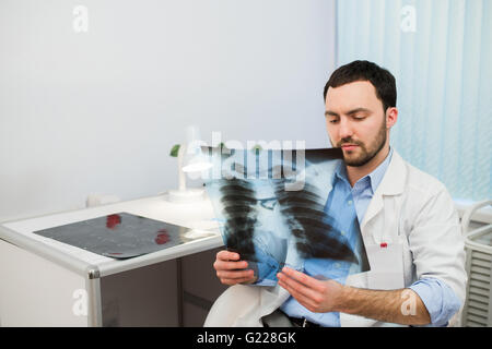 La santé et l'humeur. De graves Doctor talking to patient conserve la radiographie du thorax en mains pendant qu'assis à une table de l'hôpital. Banque D'Images