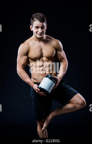 Thème : sport et musculation beau bodybuilder solide en plastique holding pot avec une protéine sèche détendre isolé sur fond noir en studio Banque D'Images