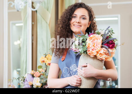 Portrait of cheerful pretty young woman holding fleuriste vase avec de magnifiques fleurs fraîches dans shop Banque D'Images