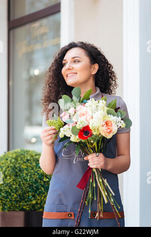 Happy charmante jeune femme florist standing in front of shop et holding bouquet Banque D'Images