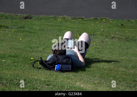 Homme ou garçon couché sur l'herbe lecture livre Kindle Reader dans le parc Kelvingrove Glasgow, Écosse, Royaume-Uni. Banque D'Images