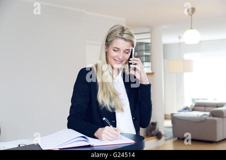 Businesswoman talking on a cell phone et l'écriture avec un stylo. home office. décor propre contemporain. Banque D'Images