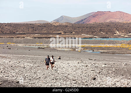 Deux personnes marchant à shingle sur plage de Playa de Janubio avec paysage volcanique, Lanzarote, îles Canaries, Espagne Banque D'Images