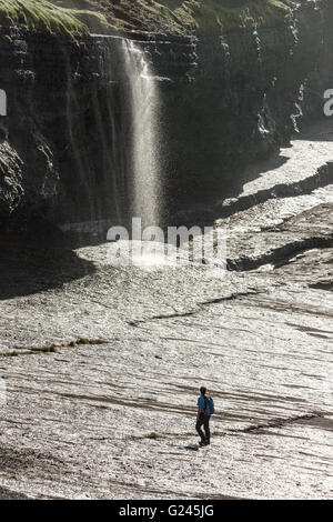 Walker sur les roches humides sous une chute d'eau sur la côte de la section de la côte de Loop Head, Comté de Clare, Irlande Banque D'Images