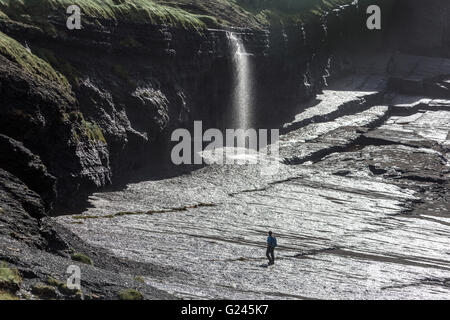 Walker sur les roches humides sous une chute d'eau sur la côte de la section de la côte de Loop Head, Comté de Clare, Irlande Banque D'Images