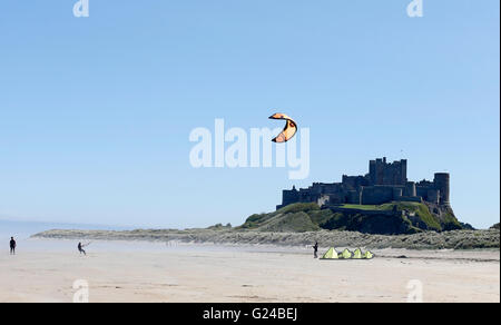 Les gens voler un cerf-volant en face de Château de Bamburgh, profiter du beau temps sur la plage de Bamburgh, Northumberland comme fret maritime dans les rouleaux. Banque D'Images